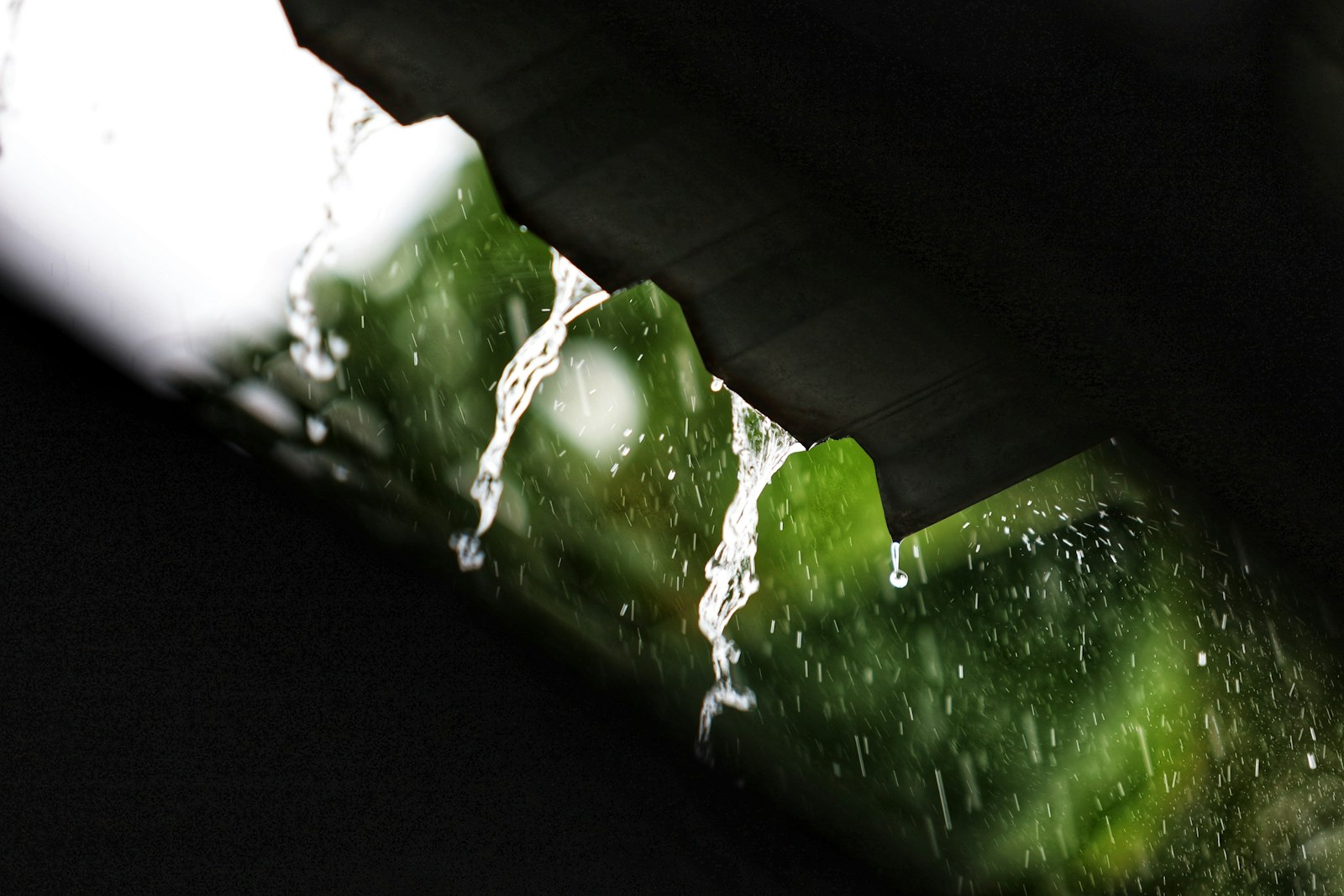 Rainwater streams from a roof edge against a green background.