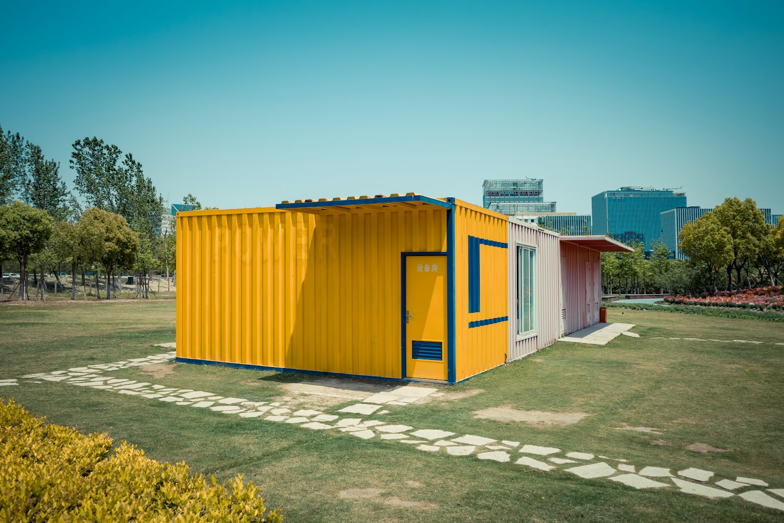 Bright yellow small container structure with glazed doorway in a grassy setting.