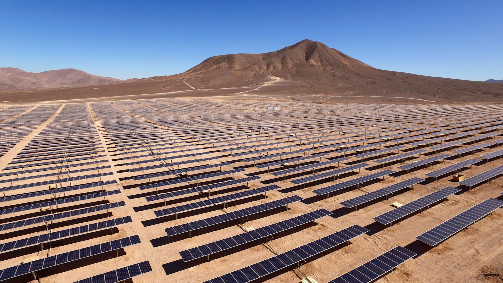 Rows of solar panels in a large photovoltaic array in a dry landscape.